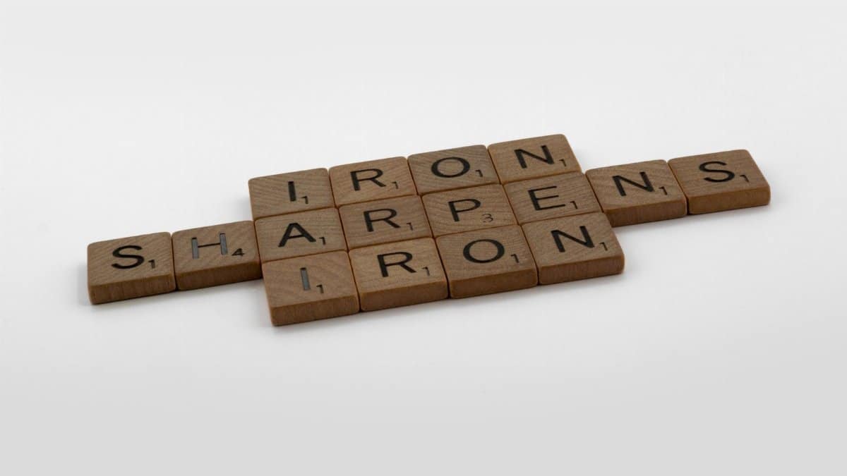 Scrabble tiles forming the phrase 'Iron Sharpens Iron' on a plain background.