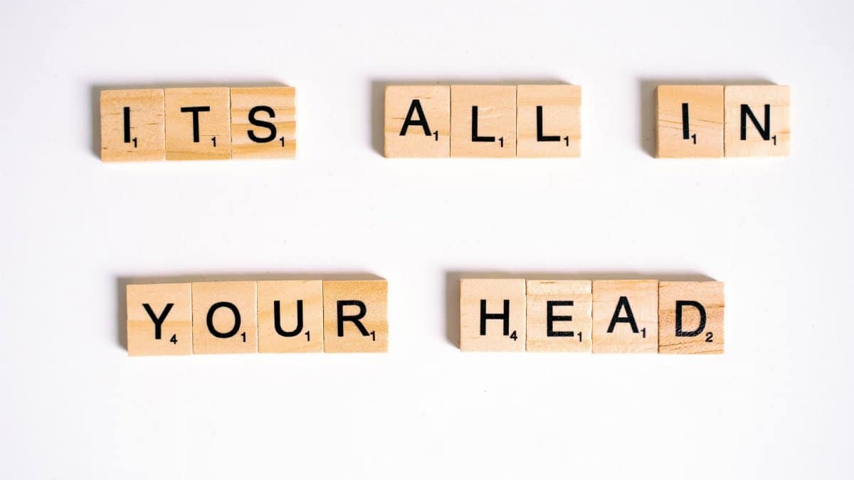 Wooden Scrabble tiles arranged to spell 'ITS ALL IN YOUR HEAD' on a white background.