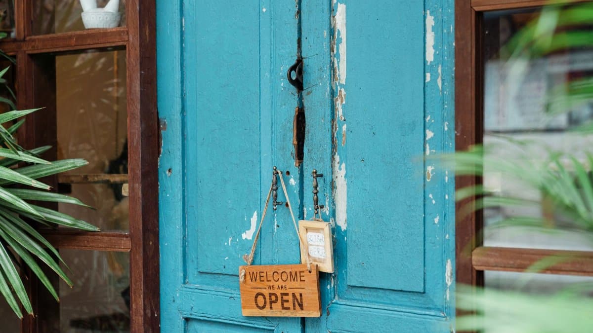A rustic blue door with a wooden welcome sign showcasing an open establishment.