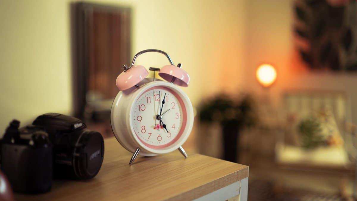 A pink vintage alarm clock on a wooden table with a cozy room background, perfect for nostalgia-themed decor.