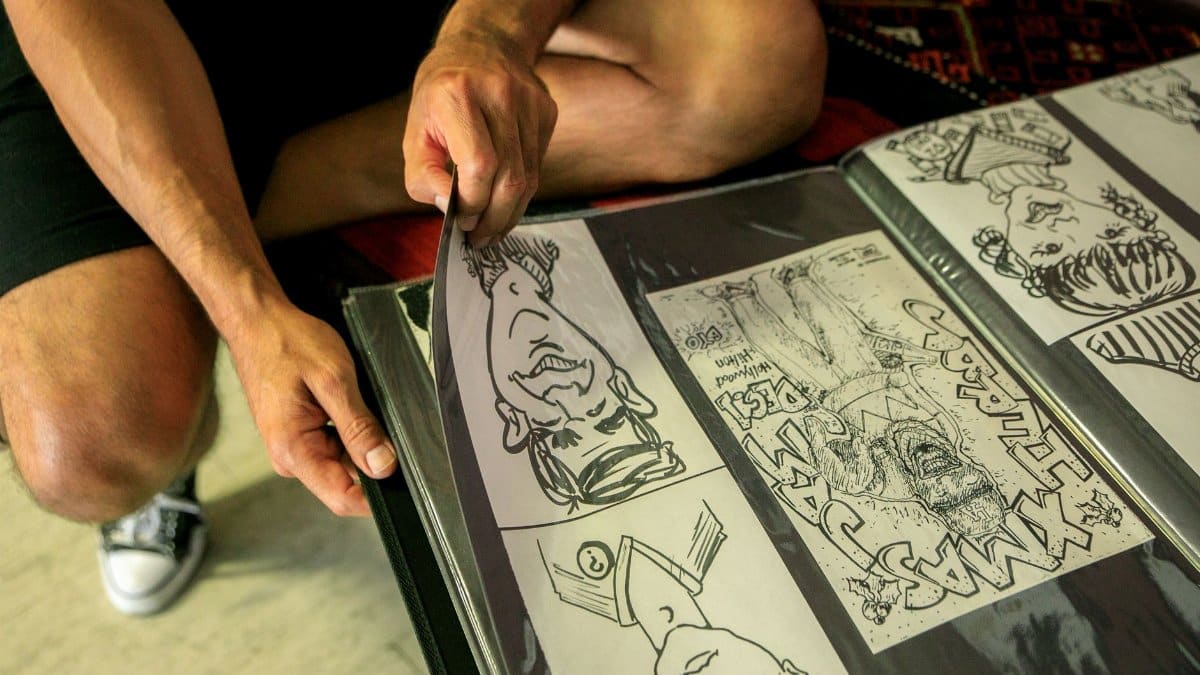 A person wearing shorts and sneakers turning pages of a comic art album, with close-up on hands and drawings.