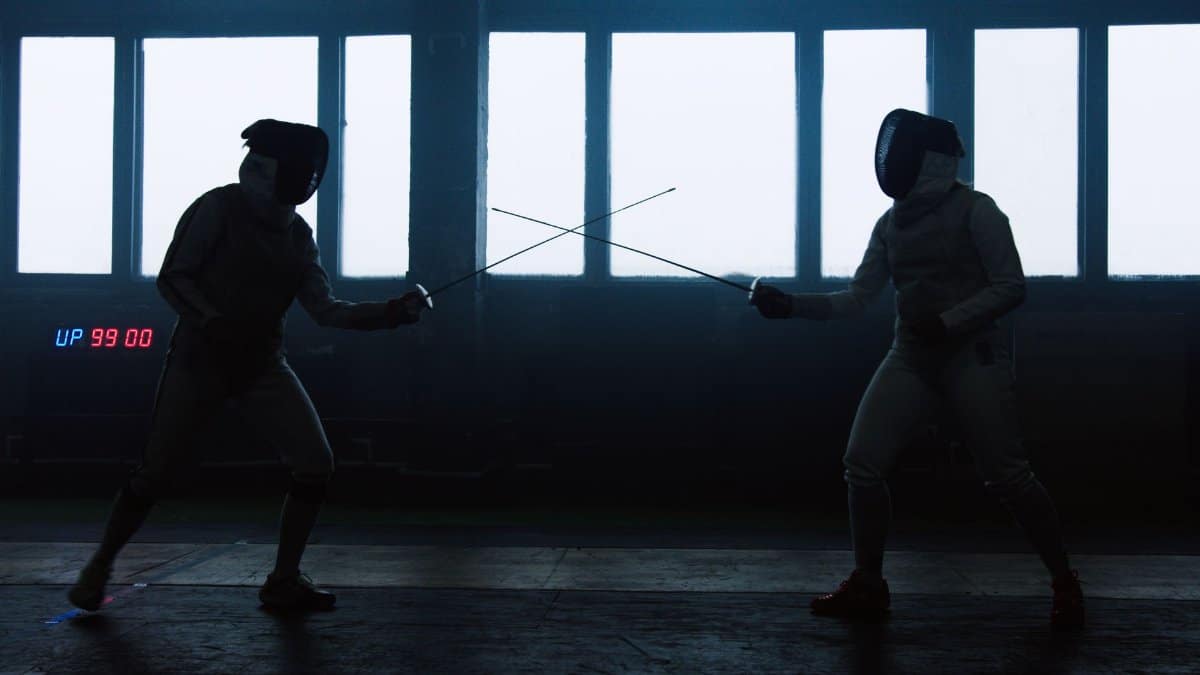 Two athletes engaged in a dynamic fencing duel inside a large hall.