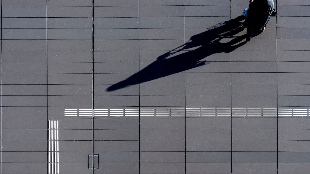Aerial shot of person casting a long shadow while walking on a tiled urban pathway.