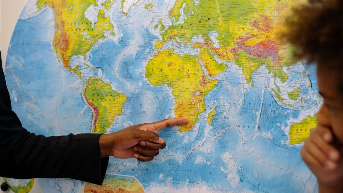 A person points to Africa on a world map, engaging with a student.