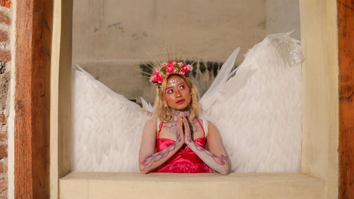 A woman in angelic costume with wings and floral headpiece posing gracefully.