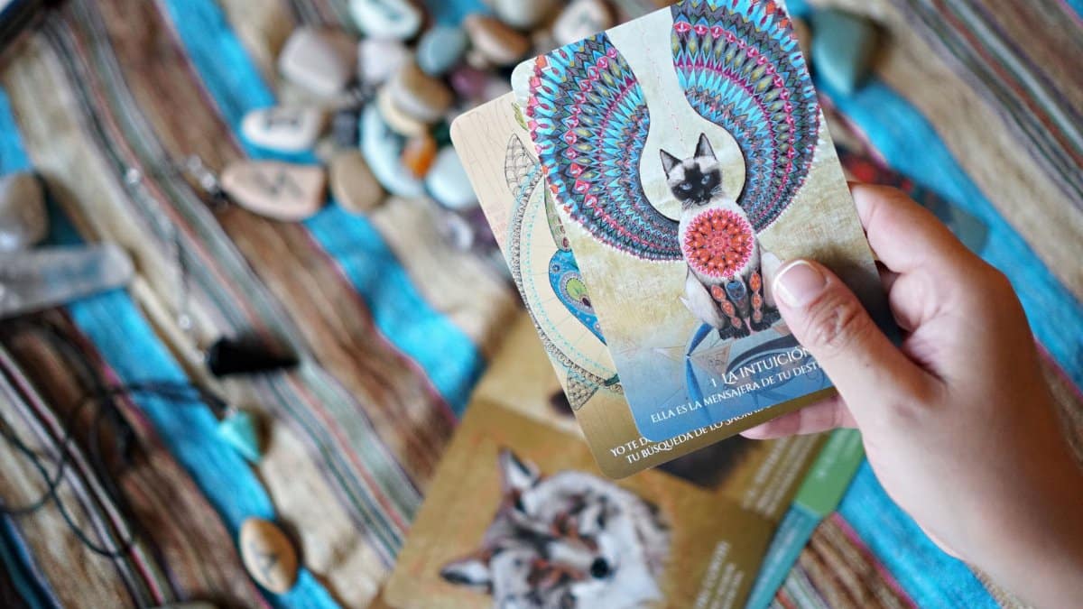Person holding tarot cards with mystical and spiritual designs, surrounded by crystals.