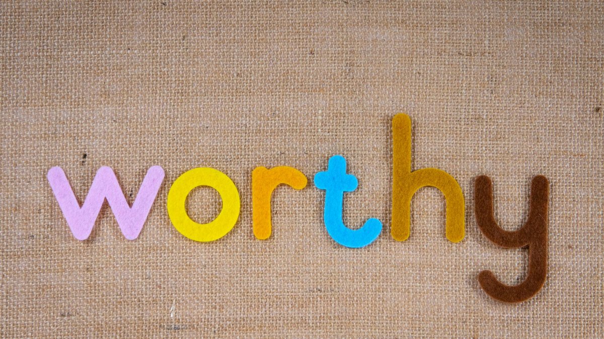 The word 'worthy' in colorful felt letters on a burlap texture, conveying positivity and value.