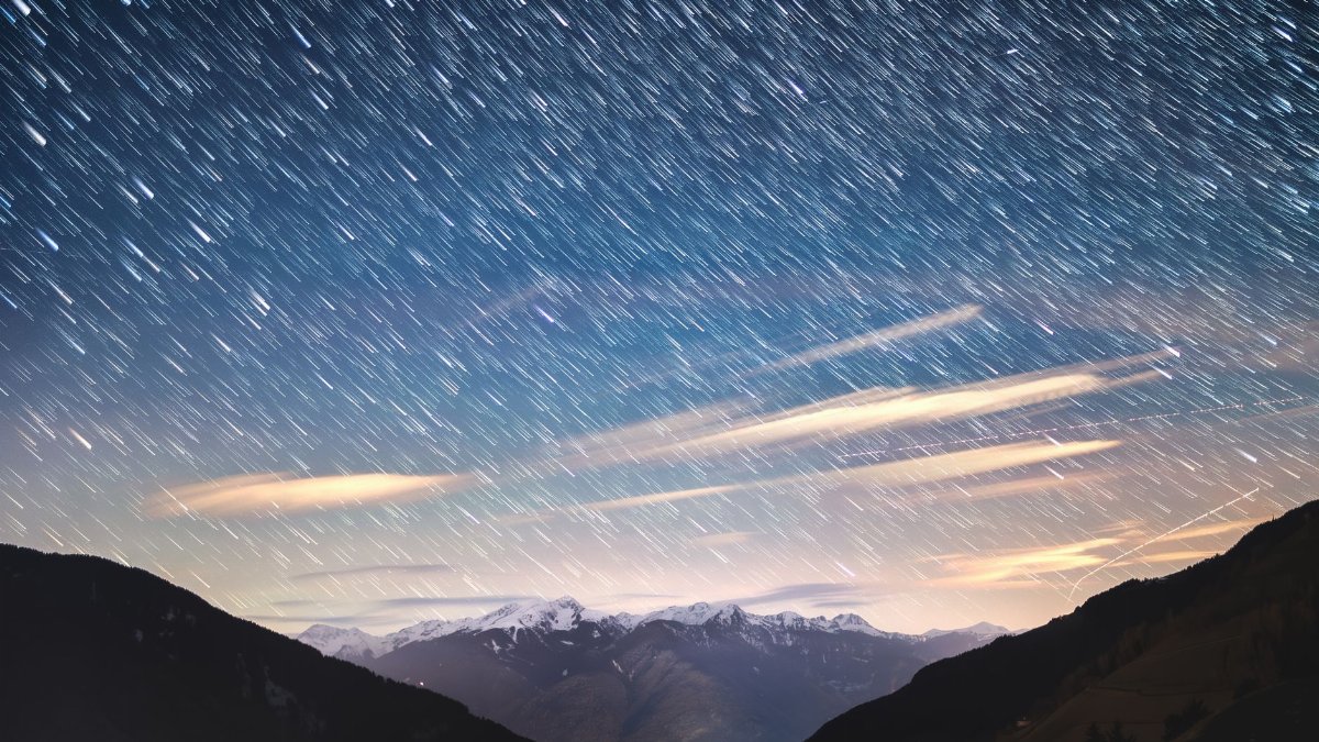 A breathtaking view of star trails over the snowy Alpine mountain range under a vibrant night sky.