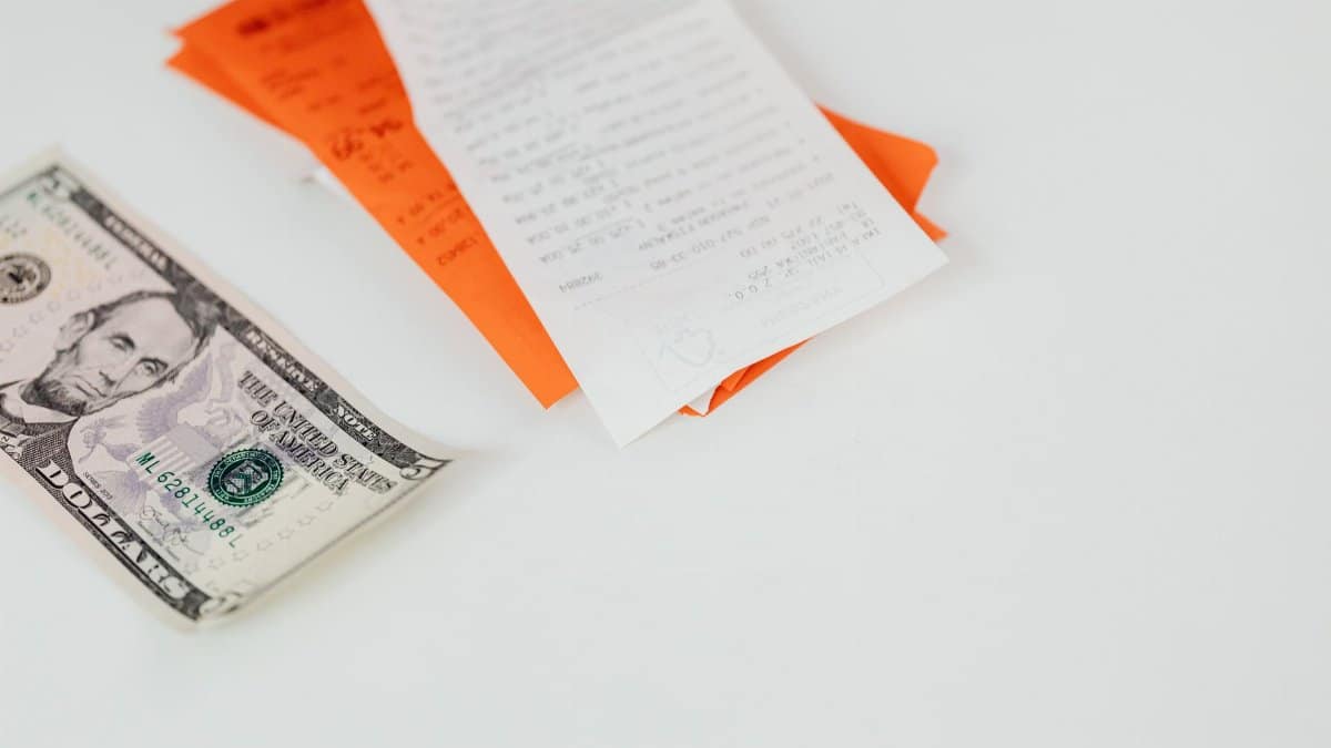 A five dollar bill and receipts on a white surface, emphasizing finance and expenses.