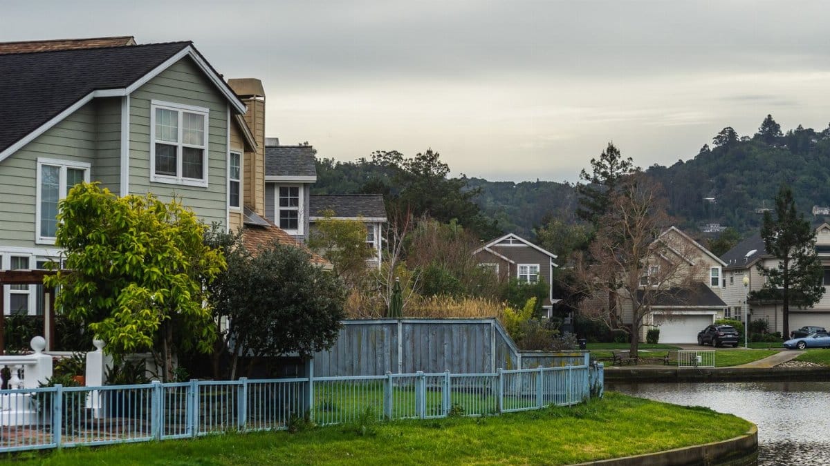 Quaint residential suburb with homes by a serene canal under a cloudy summer sky.