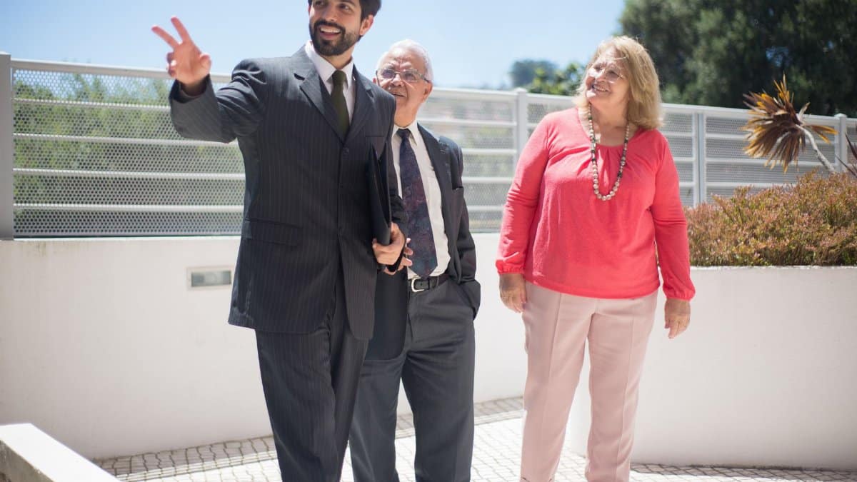 Real estate agent showcases property to a senior couple outdoors on a sunny day.