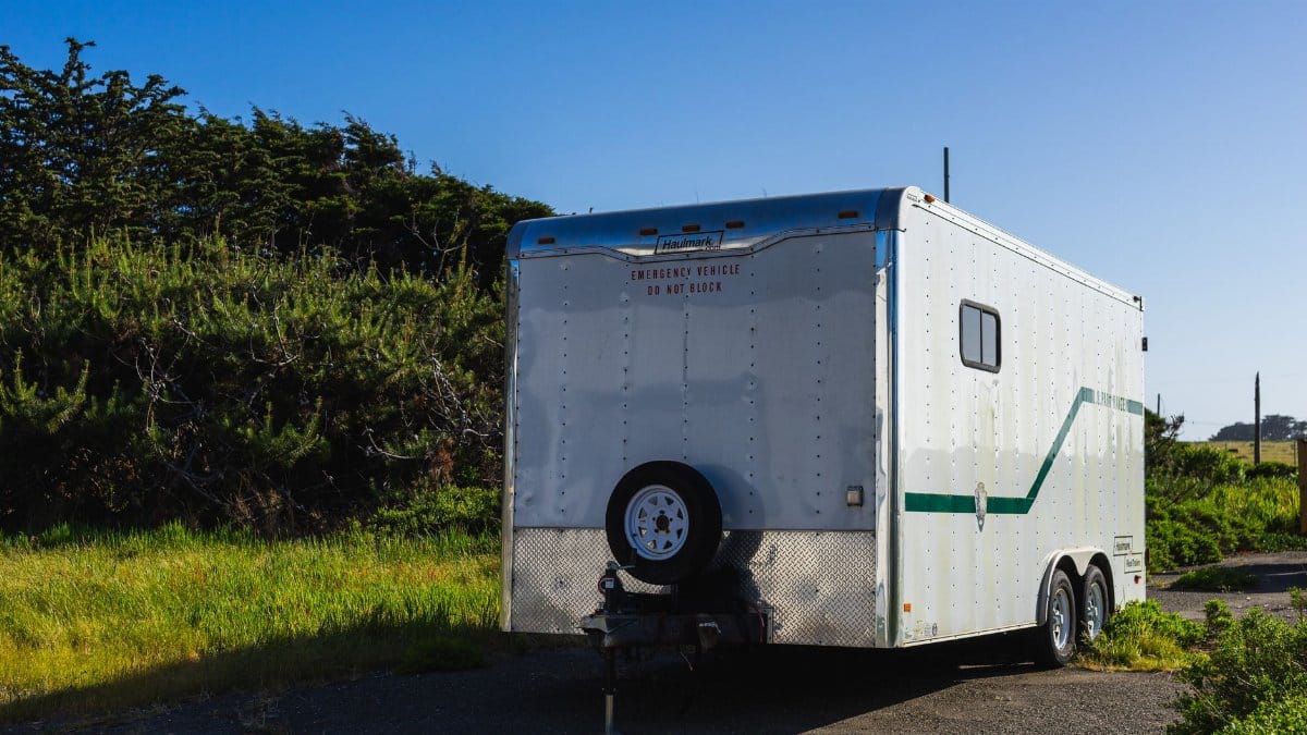 A parked white trailer surrounded by greenery under a clear blue sky in a rural area.