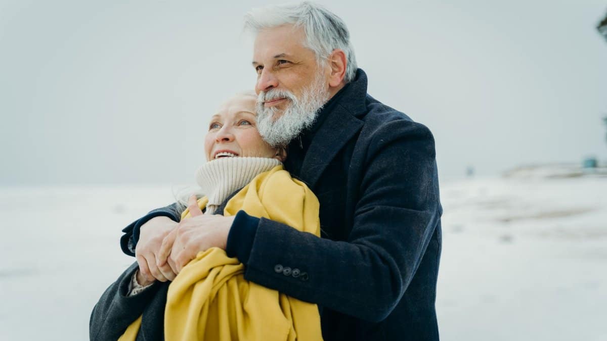 Elderly couple embracing warmly on a snowy beach. Love and connection in winter.