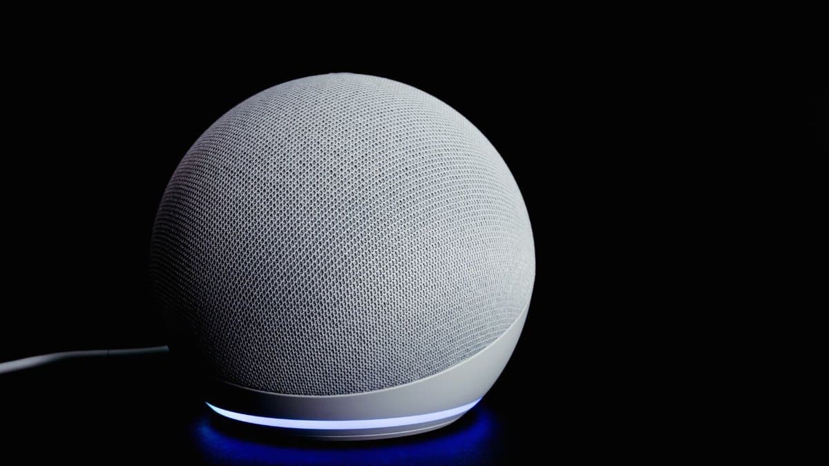Modern smart speaker device with illuminated ring, featured on a dark background.