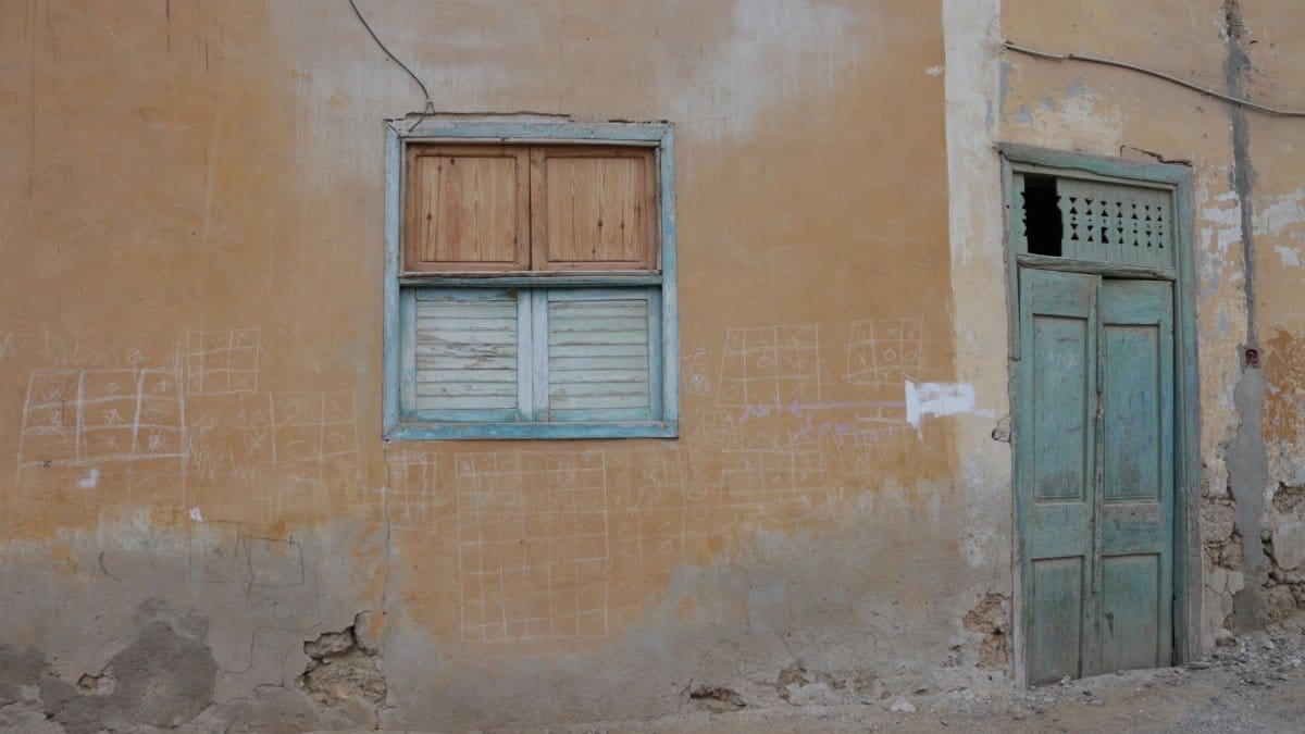 A neglected building facade featuring a window and door with visible wear and decay.
