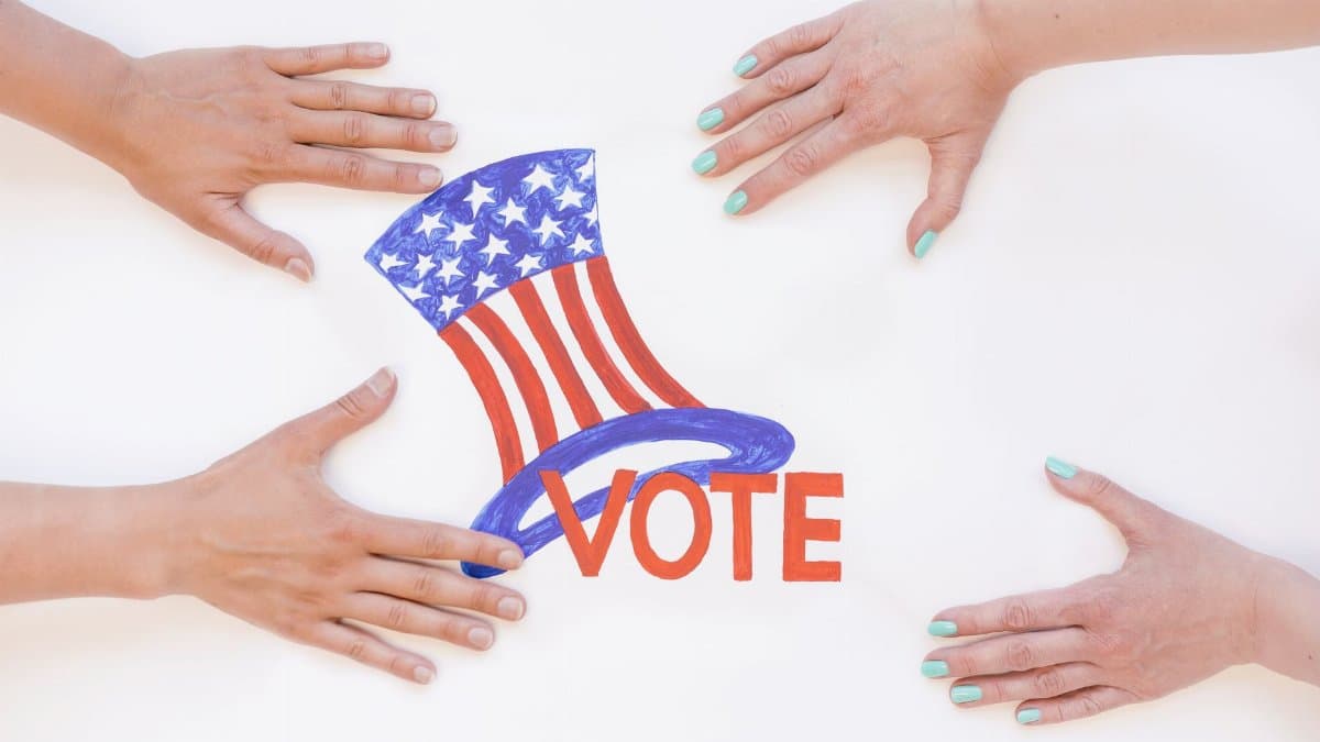 Top view of four hands around a patriotic vote sign with a hat.