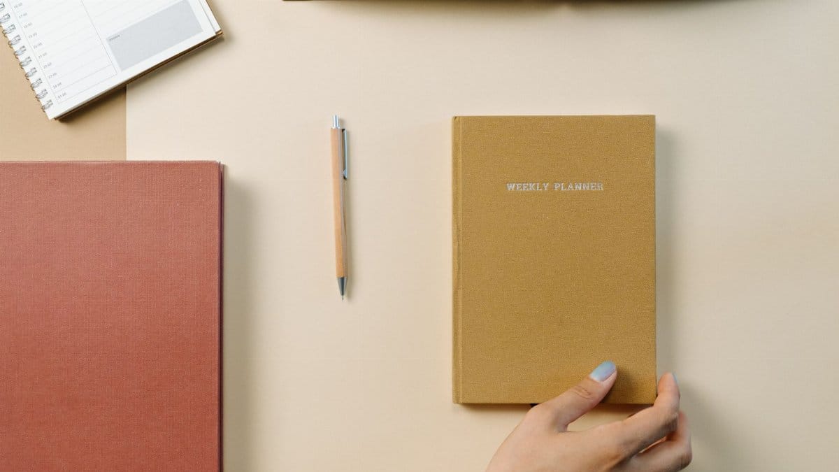 Top-down view of a desk with a weekly planner, notebook, and pen promoting organization.