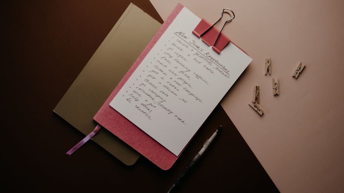 Aesthetic flat lay of a New Year's resolution list on a notepad with warm lighting and writing materials.