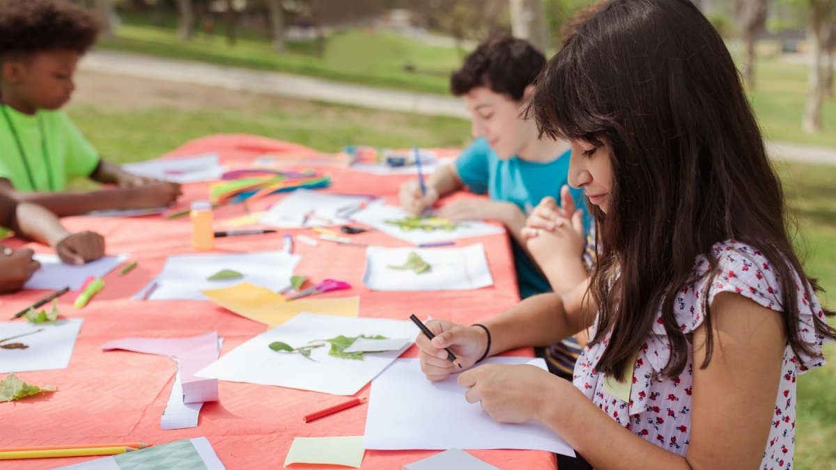 Children participating in outdoor art activities, creating crafts and drawings on a sunny day.