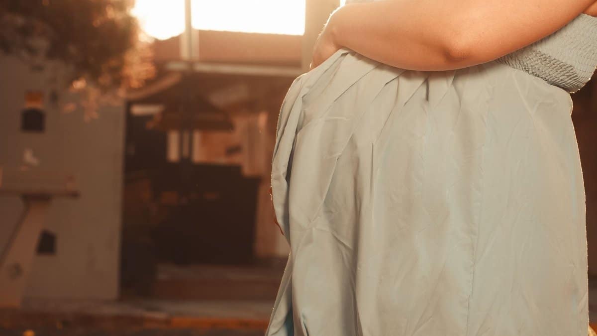 Outdoor portrait of a pregnant woman gently holding her belly with warm sunlight in the background.