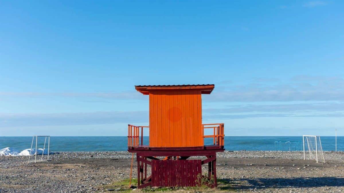 Orange wooden lifeguard tower located at seaside under blue sky in summer on sunny day