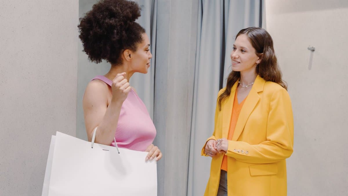 Two women discussing fashion and style in a clothing store setting, indoors.