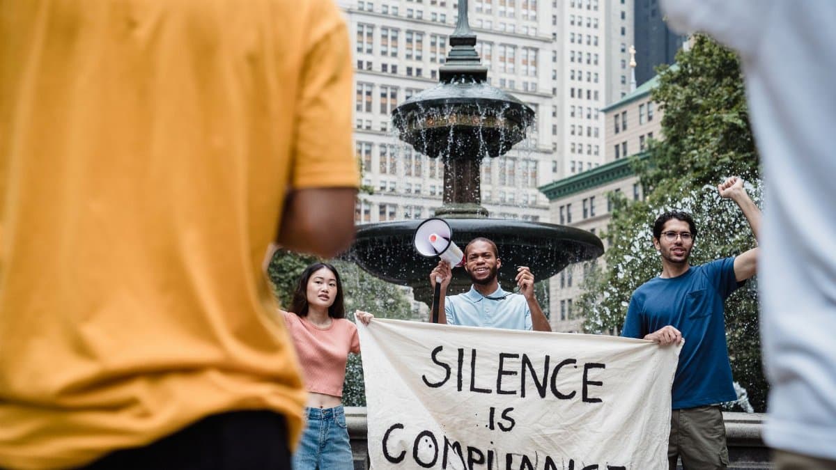 A diverse group of protesters holding a banner and megaphone in a city square advocating for social change.