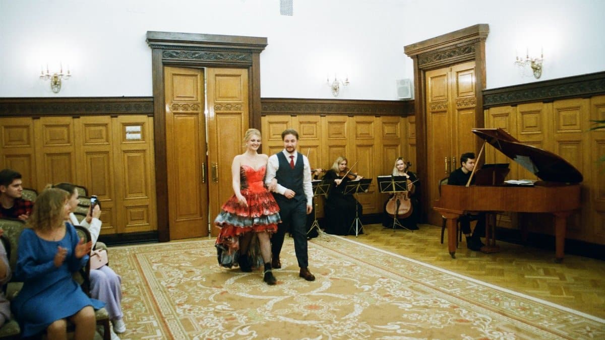 Elegant couple walks in formal reception with string quartet and guests applauding.