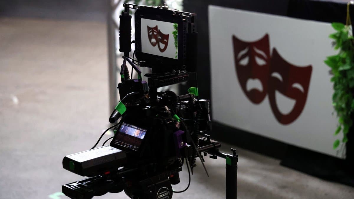 Professional film camera capturing theater performance showing drama and comedy masks.