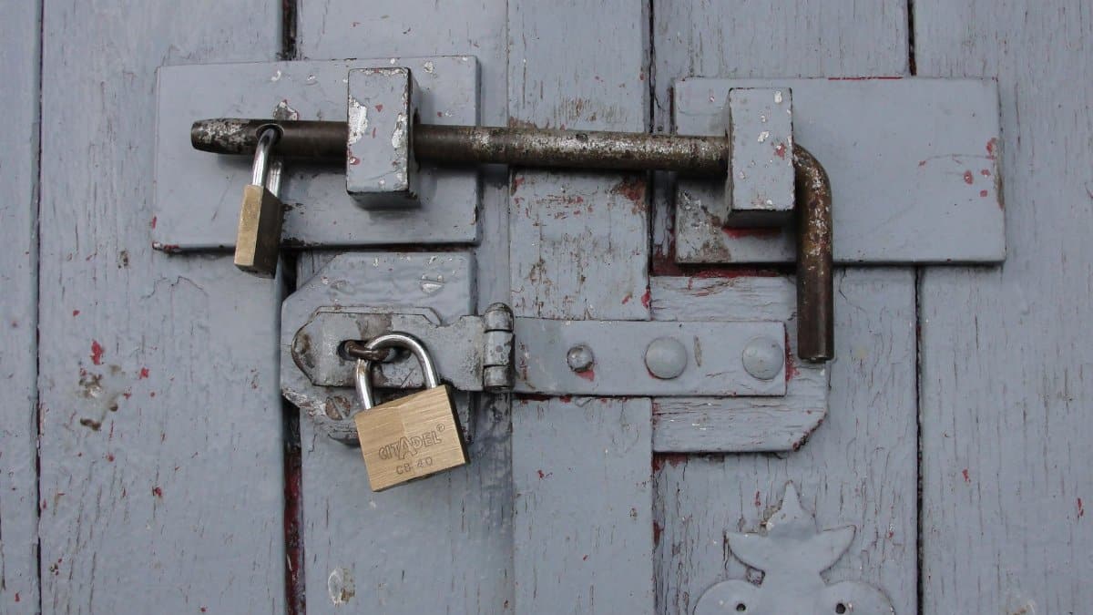 Detailed view of a securely locked wooden door with weathered brass padlocks.