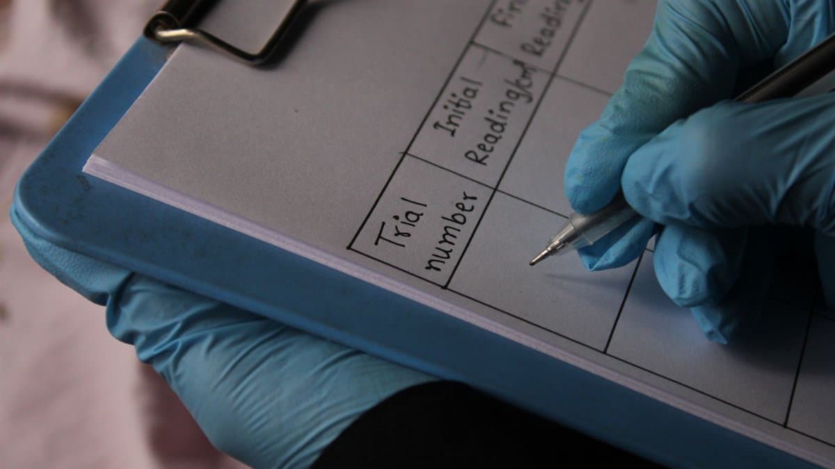 Person wearing gloves writing on clipboard with trial data sheet.