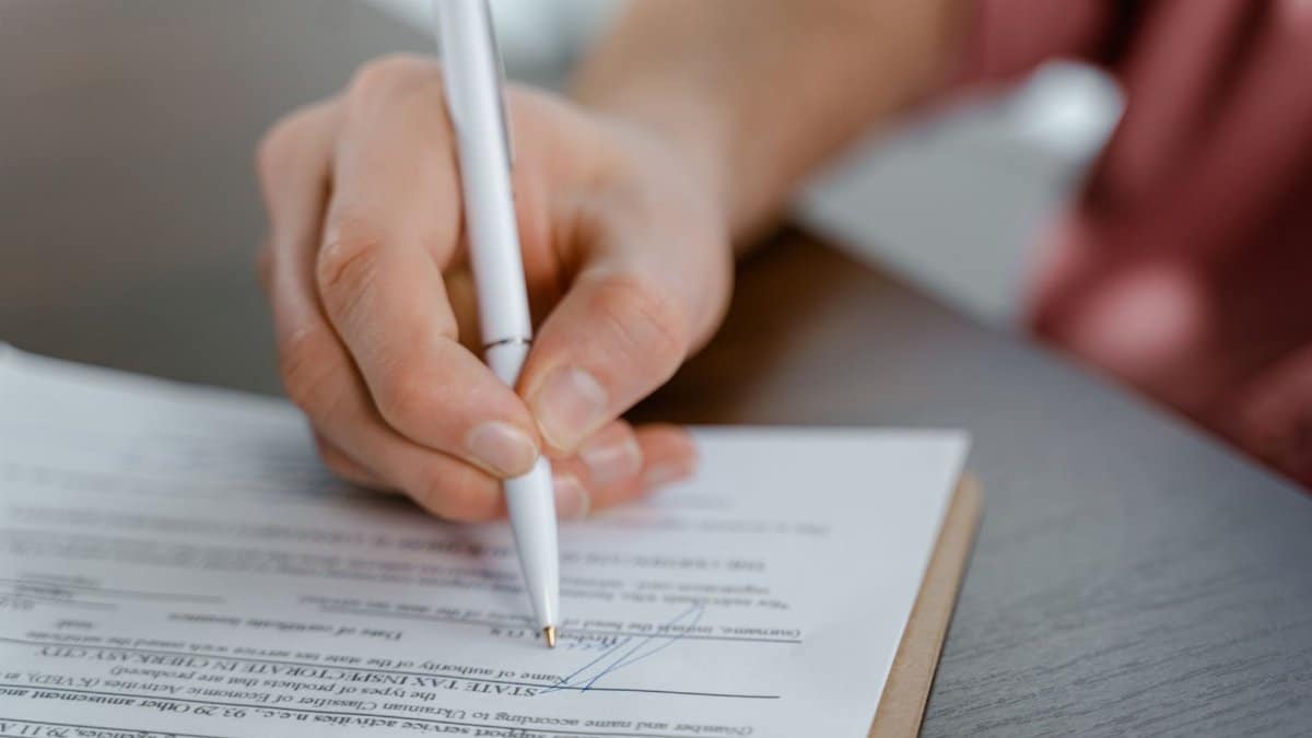 Detailed view of a hand writing a signature on an official document with a ballpoint pen.