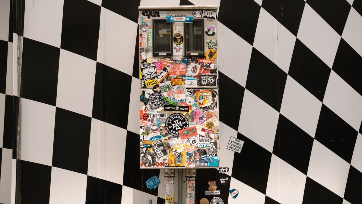 A sticker-covered vending machine against a checkered wall in Tokyo, Japan.