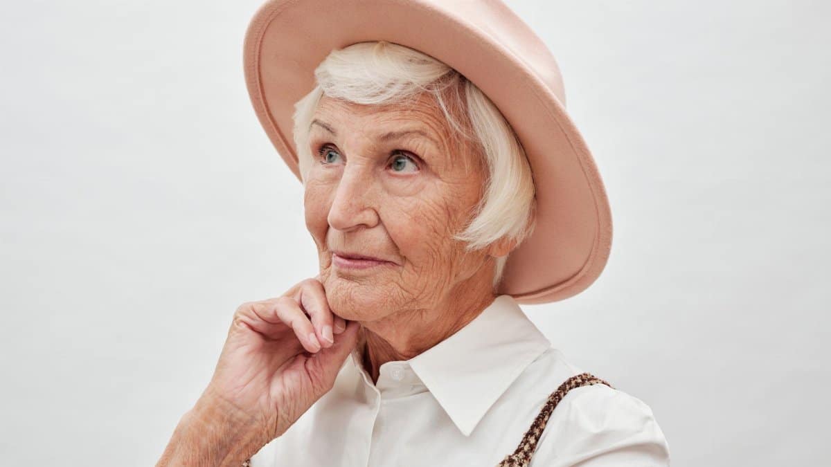 Elegant senior woman wearing a pink hat poses thoughtfully. Ideal for topics like fashion, age diversity, and elegance.