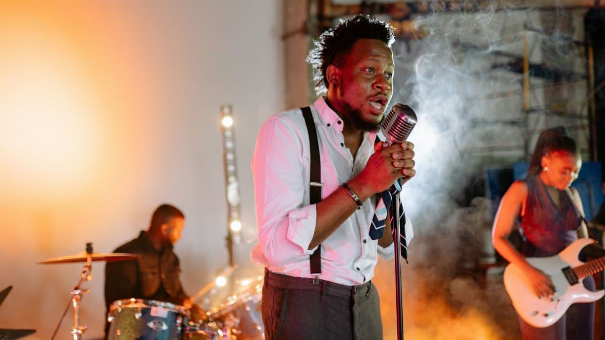 A vibrant indoor band performance featuring a singer, drummer, and guitarist in action.