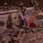 A partially burnt 100 dollar bill lies among ashes, symbolizing loss or financial ruin.