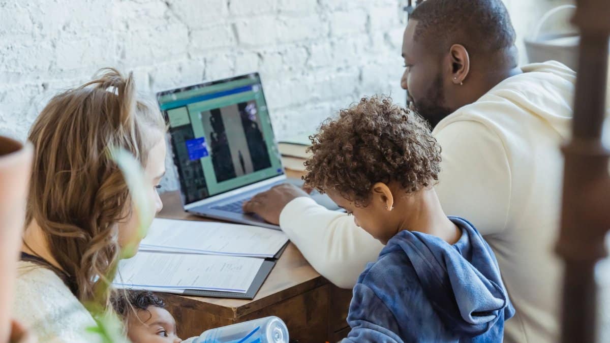 High angle of African American dad watching laptop working near son playing toys and mother feeding little infant