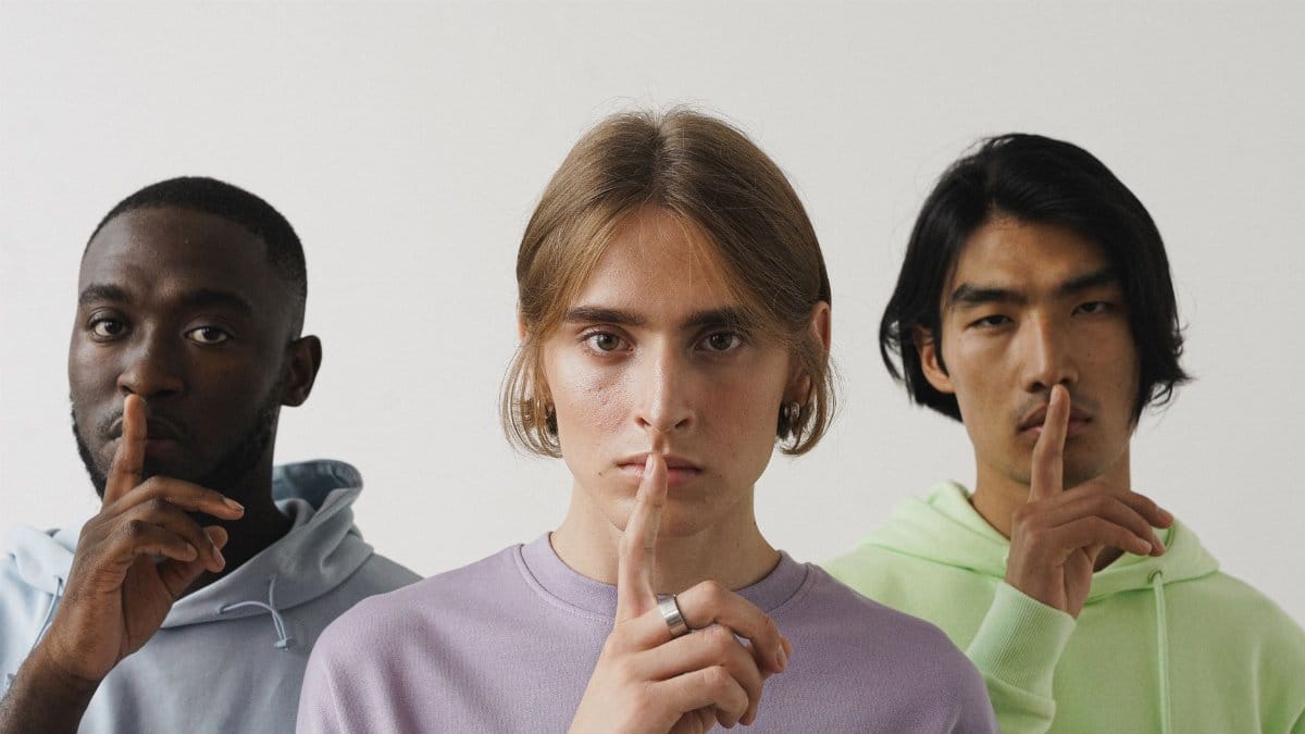 Three young adults making a shushing gesture in a studio setting, highlighting diversity.