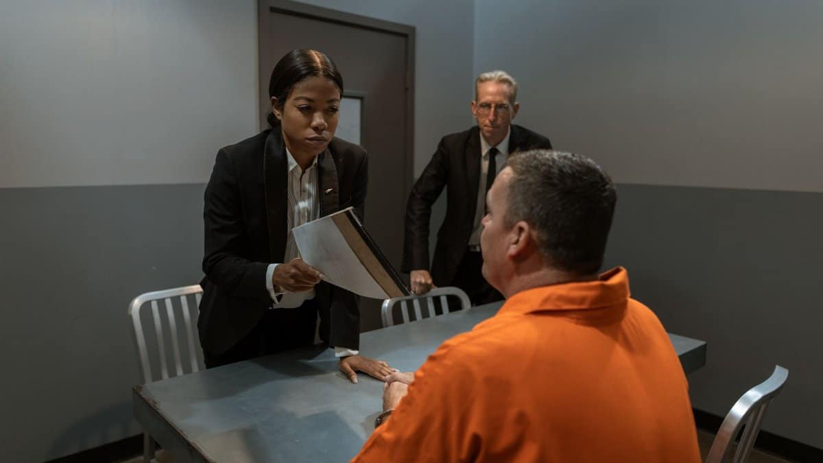 A tense interrogation scene in a prison room with officials and a prisoner.