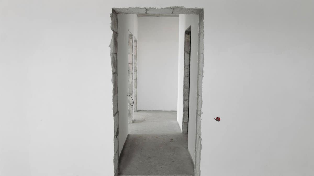Interior view of a simple white corridor in an unfinished building, showing raw construction details.