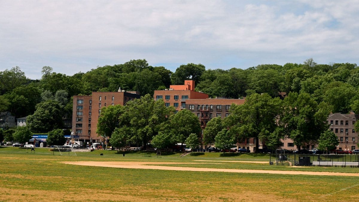 A scenic view of a park with residential buildings and lush trees under a cloudy sky.