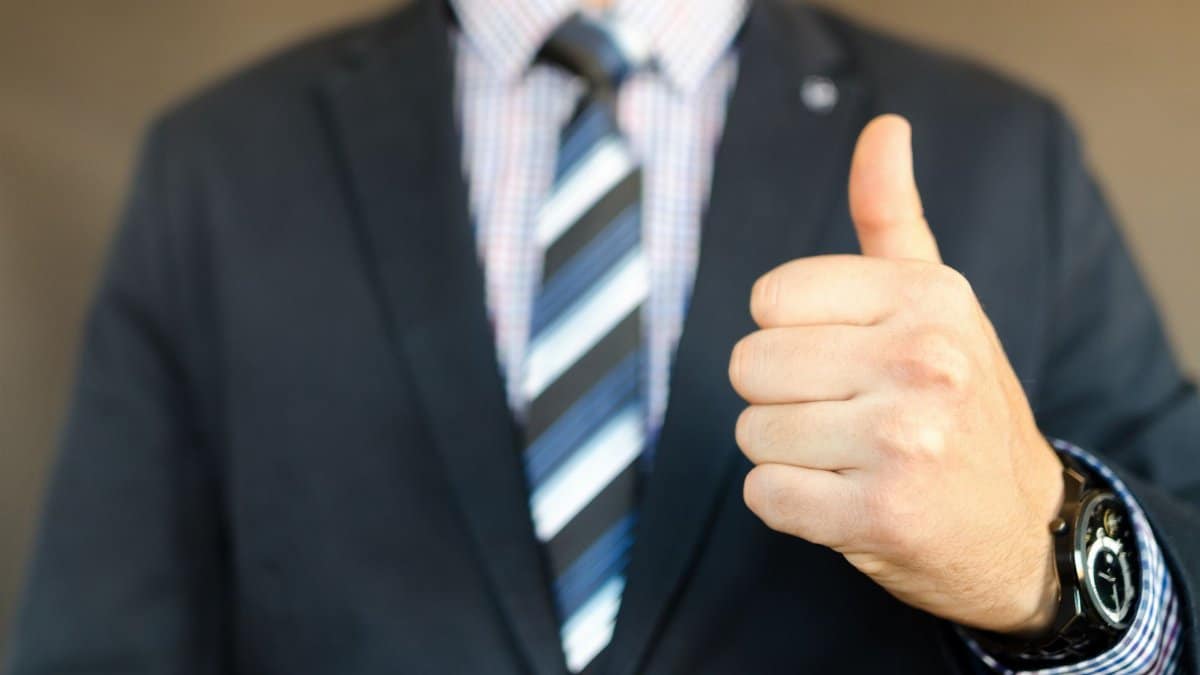 Close-up of a businessman in a suit giving a thumbs up gesture, symbolizing success.