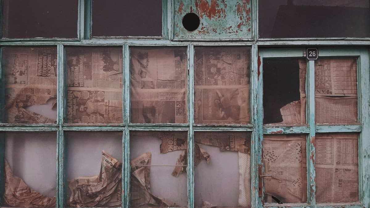 Urban decay of a vintage building with newspaper-covered windows and peeling paint.