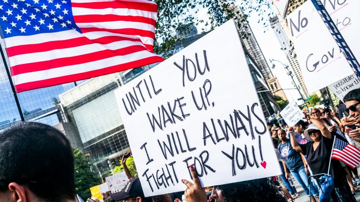 Diverse crowd protesting in New York City with American flags and placards advocating for change.