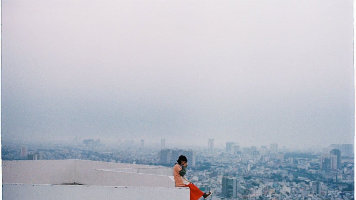 A woman sits poised on a building's edge, high above a sprawling cityscape.