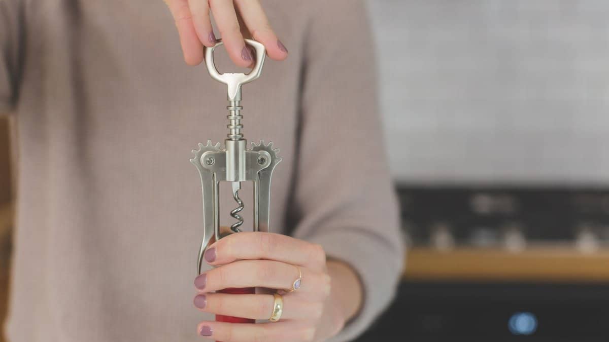 Close-up of a woman using a corkscrew to open a wine bottle indoors.