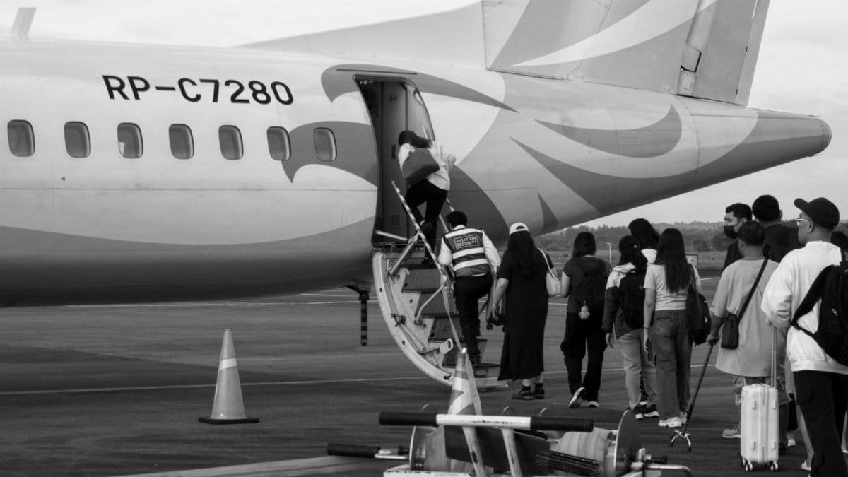 Black and white photo of people boarding a small propeller airplane on the tarmac.