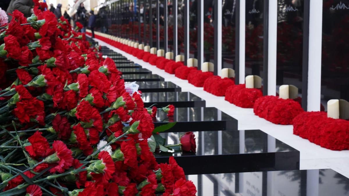 A solemn memorial wall adorned with red carnations and candles during the daytime.