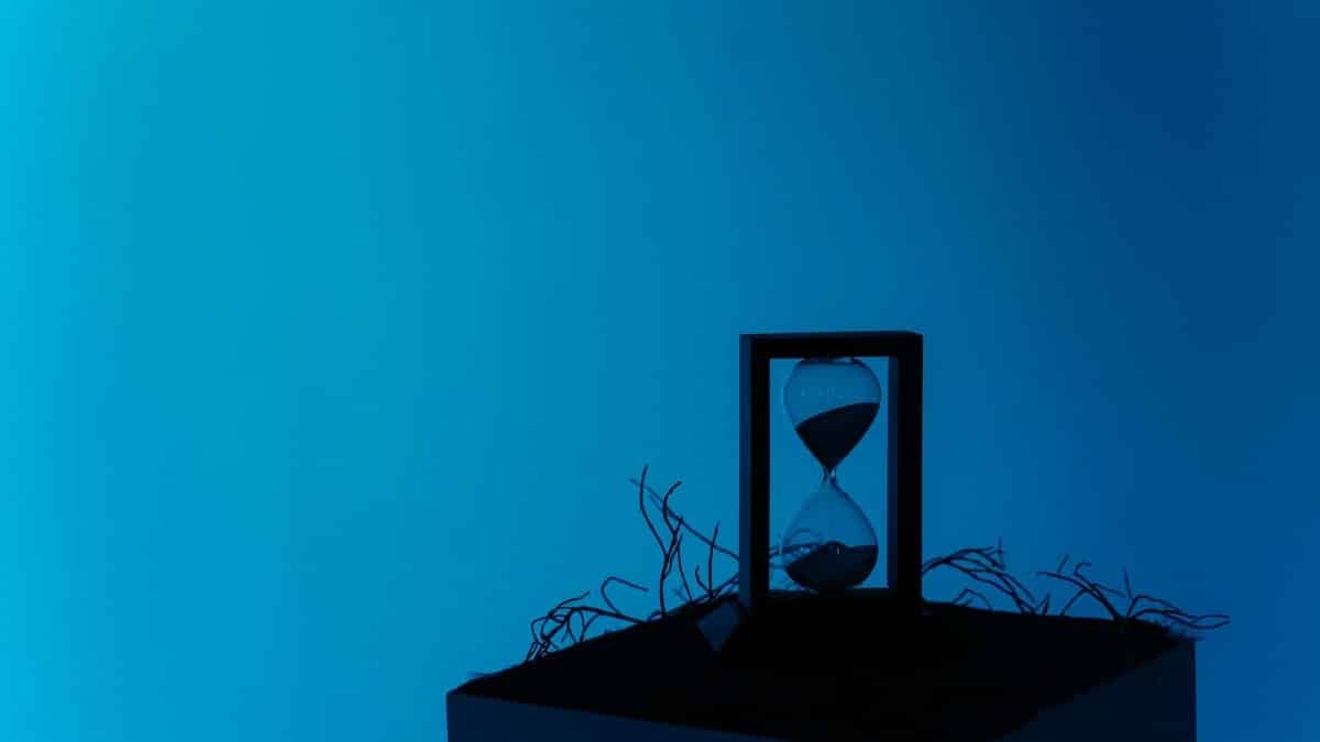 A minimalist hourglass set against a vibrant blue backdrop, representing the passage of time.