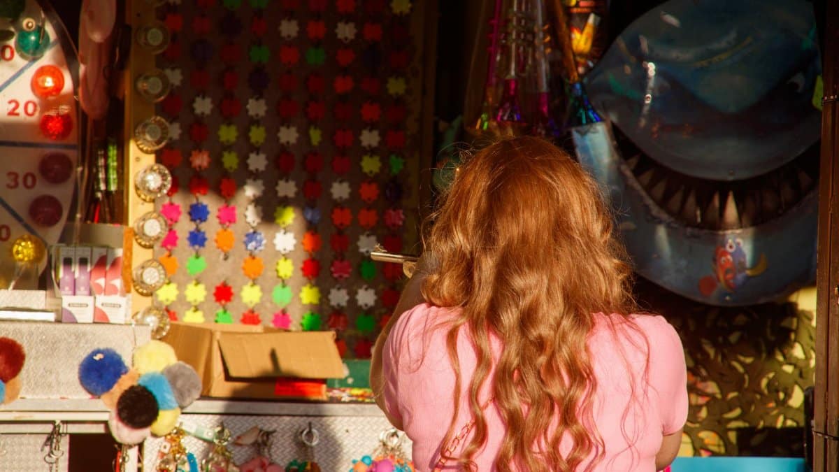 Young girl playing a carnival game at a brightly lit midway stall with toys and decorations.